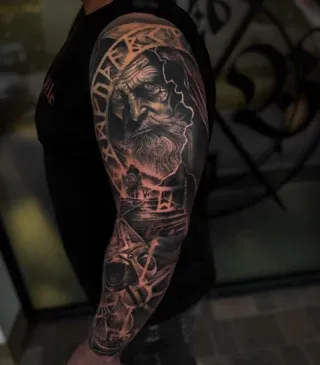 Großflächiges Black-and-Grey-Tattoo mit Porträt und grafischen Formen auf einem Arm.