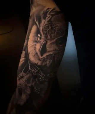 Dunkles, detailliertes Eulen-Tattoo auf einem Unterarm.